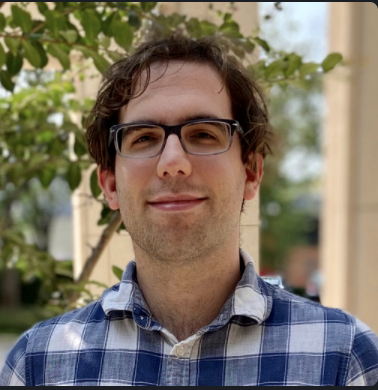 headshot man in black and white checkered shirt with short brown hair and glasses