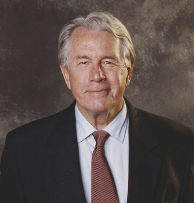 Portrait shot of Ken Roberts, allum and philanthropist in a dark suit, white shirt and dark red tie