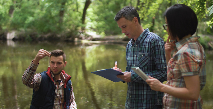 A professor and two students testing water quality in a creek