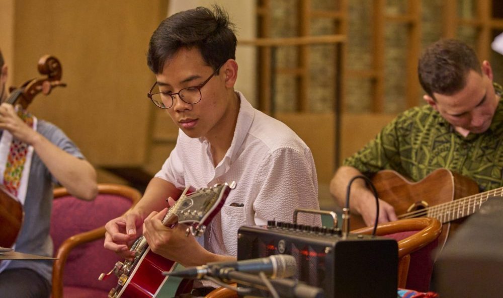 Student playing guitar during graduation worship.