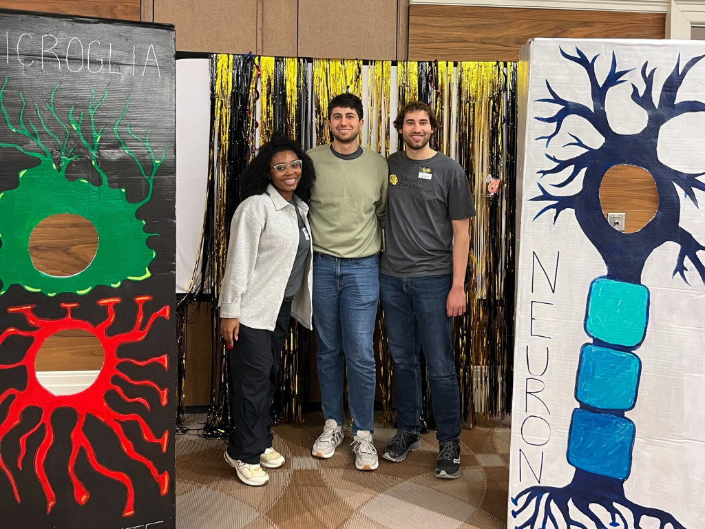 Attendees of the 2025 Brain Blast event. Four attendees sitting behind a booth smiling at the camera.