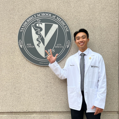 A man in a white coat points at the seal of Vanderbilt School of Medicine.