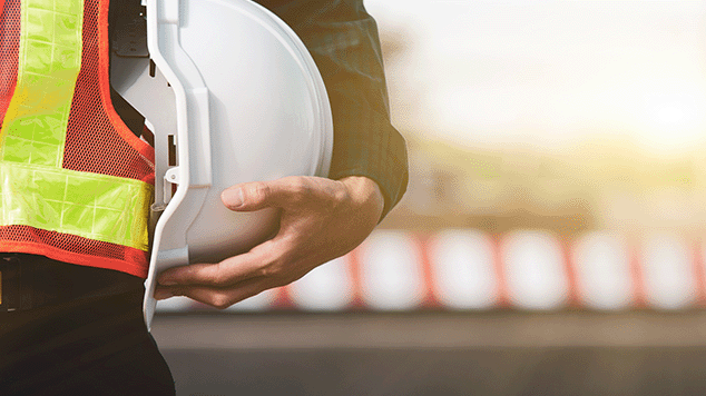 construction worker wearing reflective vest holds white hard hat
