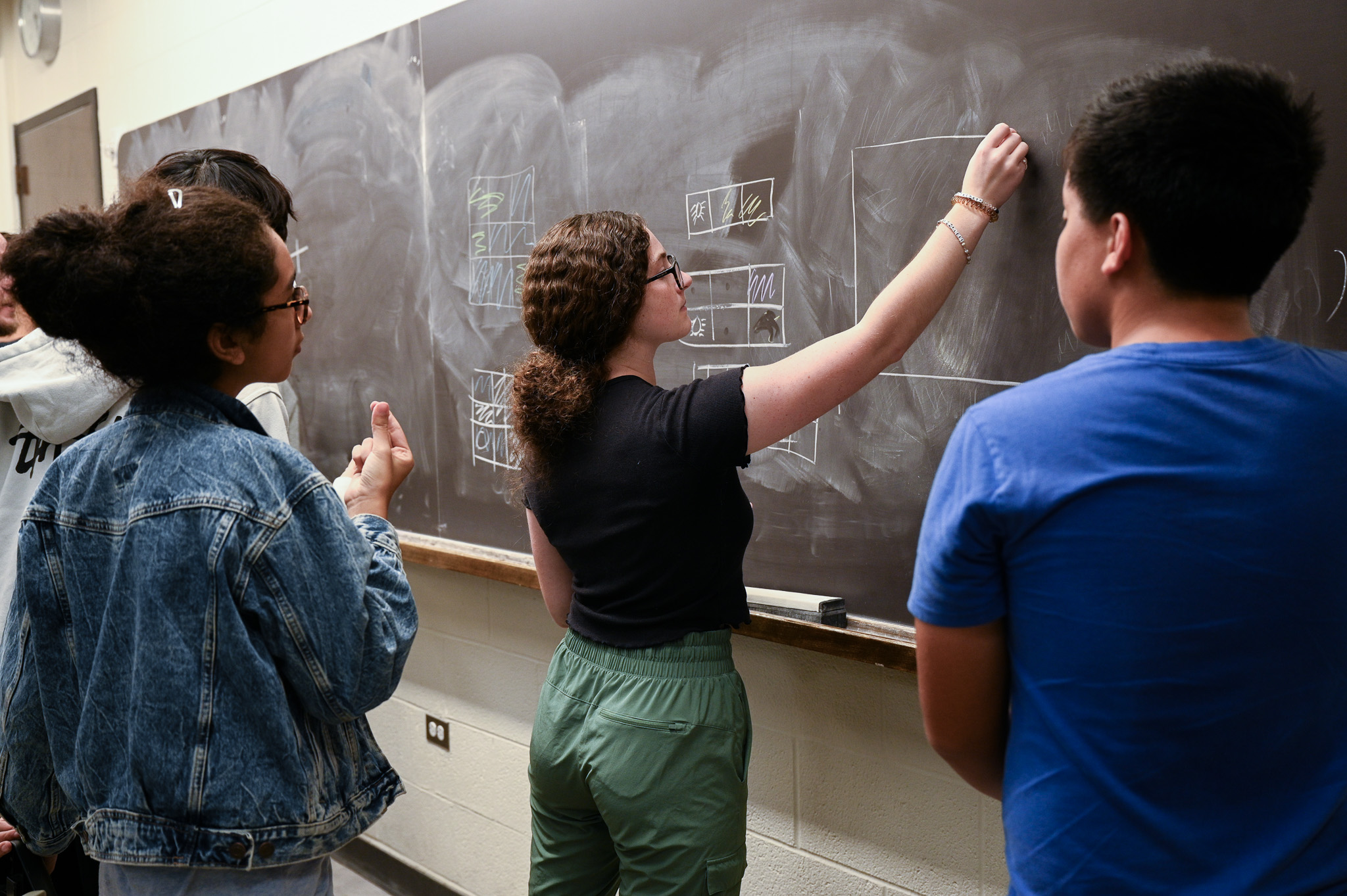 Students working out a math problem on a chalkboard.