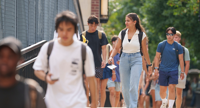Photo: Vanderbilt University students walking along a campus pathway on a sunny day, carrying backpacks and engaging with one another.
