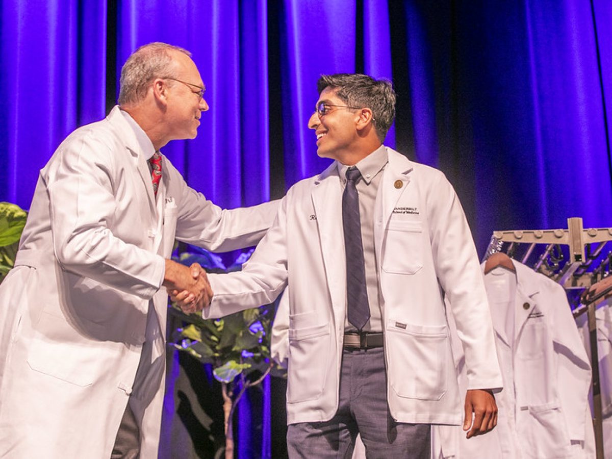 A new medical student shakes the dean's hands after donning his white coat.