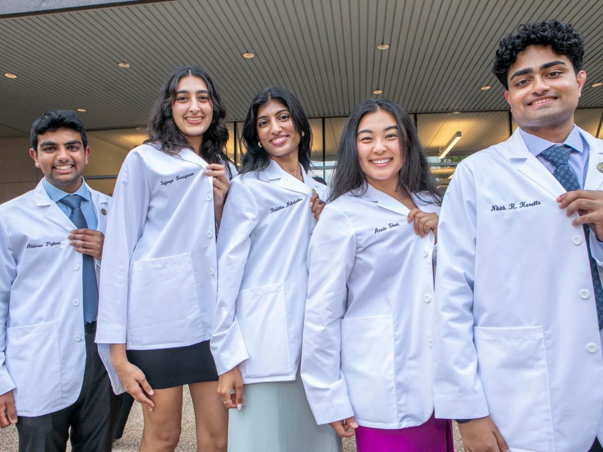 Five VUSM medical students, smiling and holding open their white coats to show their embroidered names.