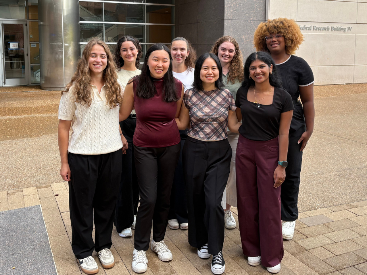 A group of seven smiling VUSM genetic counselilng students smiles in front of the medical research building.