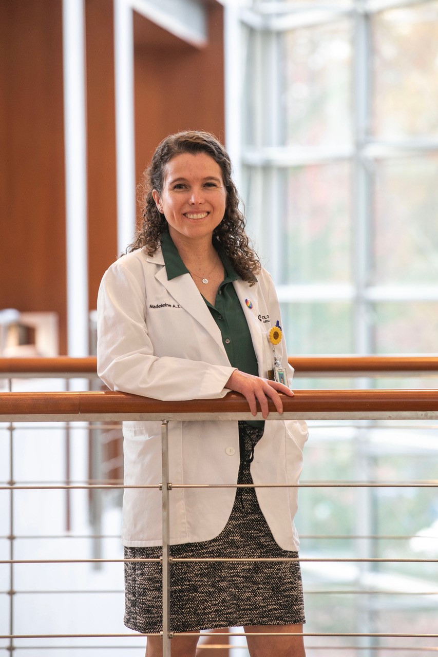A woman stands behind a rail. She's wearing a white coat.
