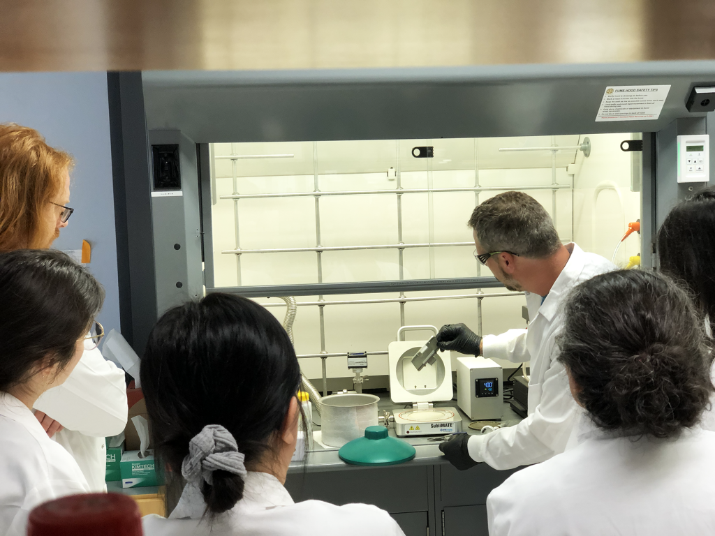AIMS attendees observe a scientist working at a fume hood at a workshop.