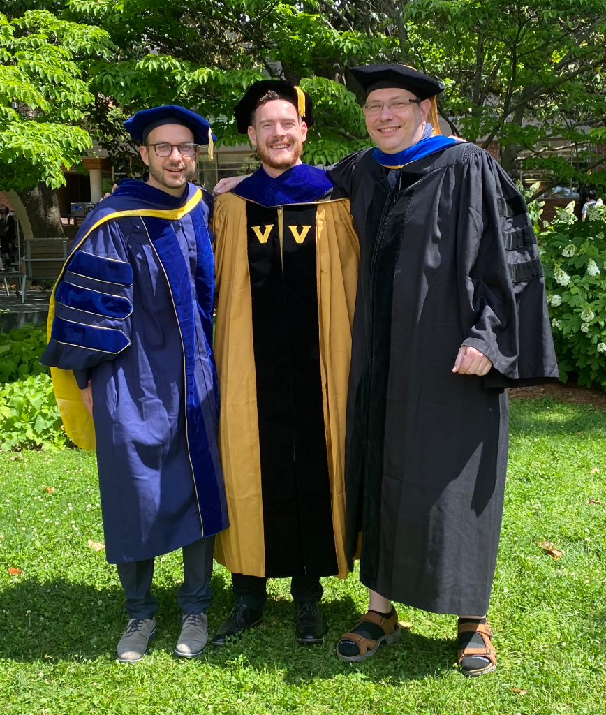 Lars Plate (left), Eli McDonald (middle), and Jens Meiler in doctoral regalia standing in front of some trees on campus.