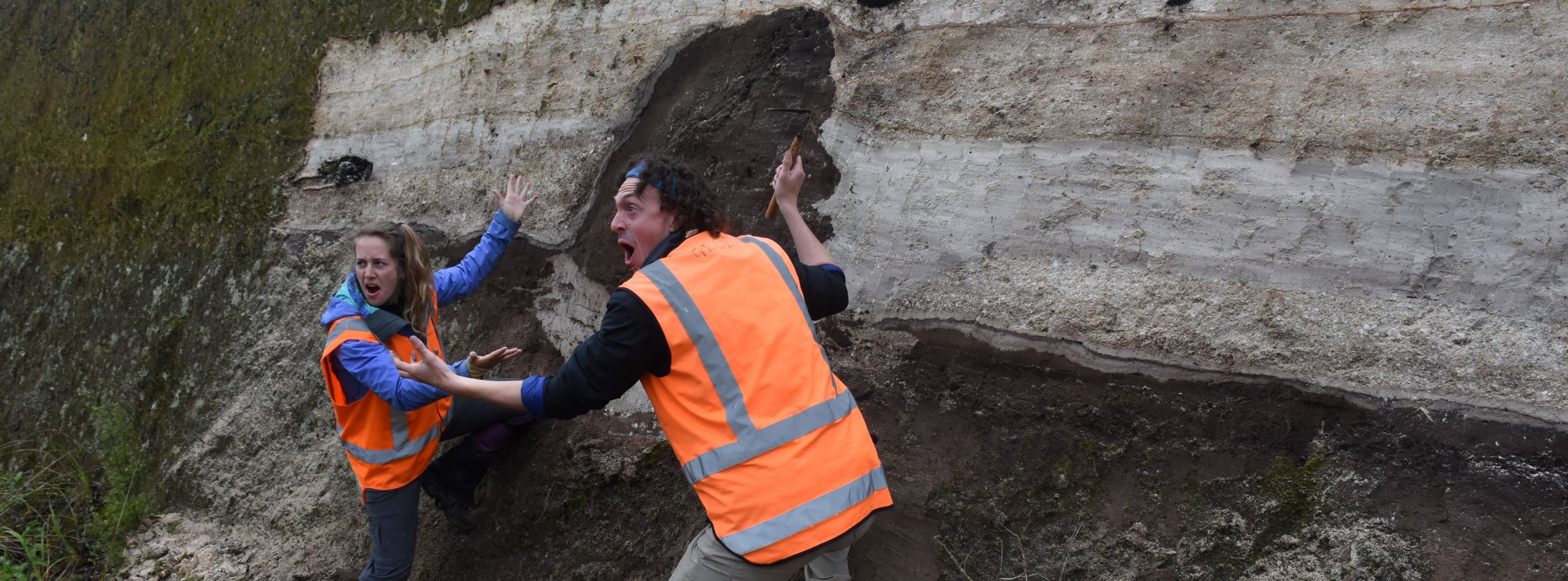Lydia Harmon and Brad Pitcher gesturing excitedly at a hole in a large geologic formation
