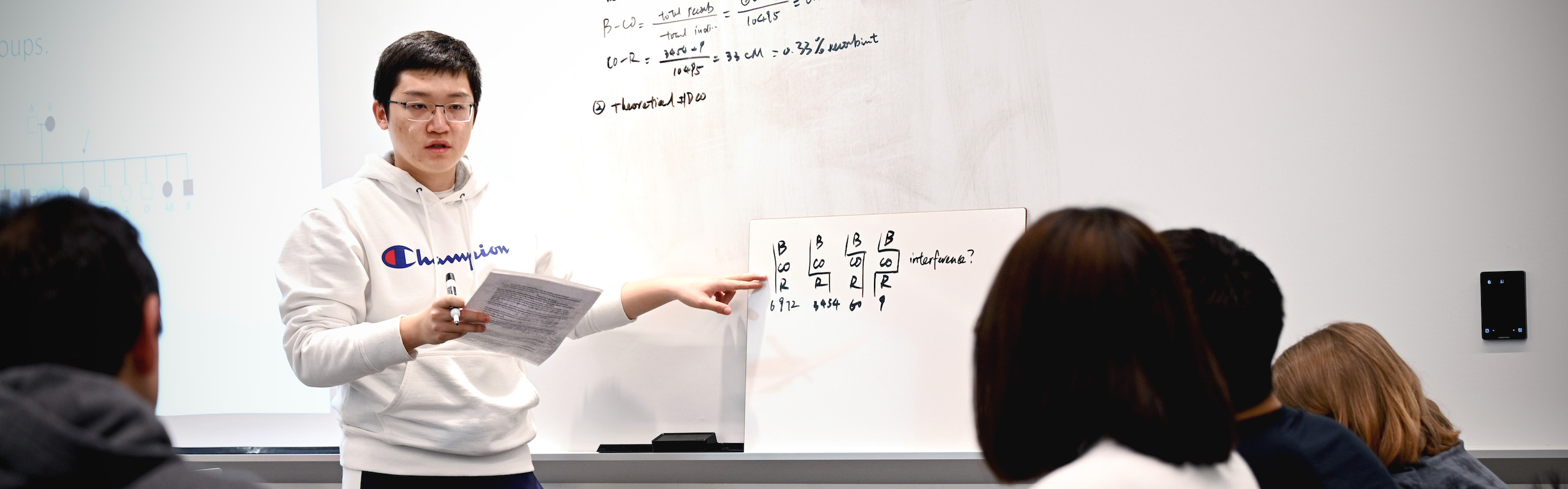 Student standing in front of class and pointing to white board