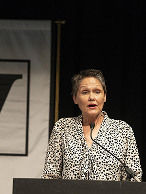 Joy Calico standing at a lectern and speaking with a Vanderbilt flag behind her