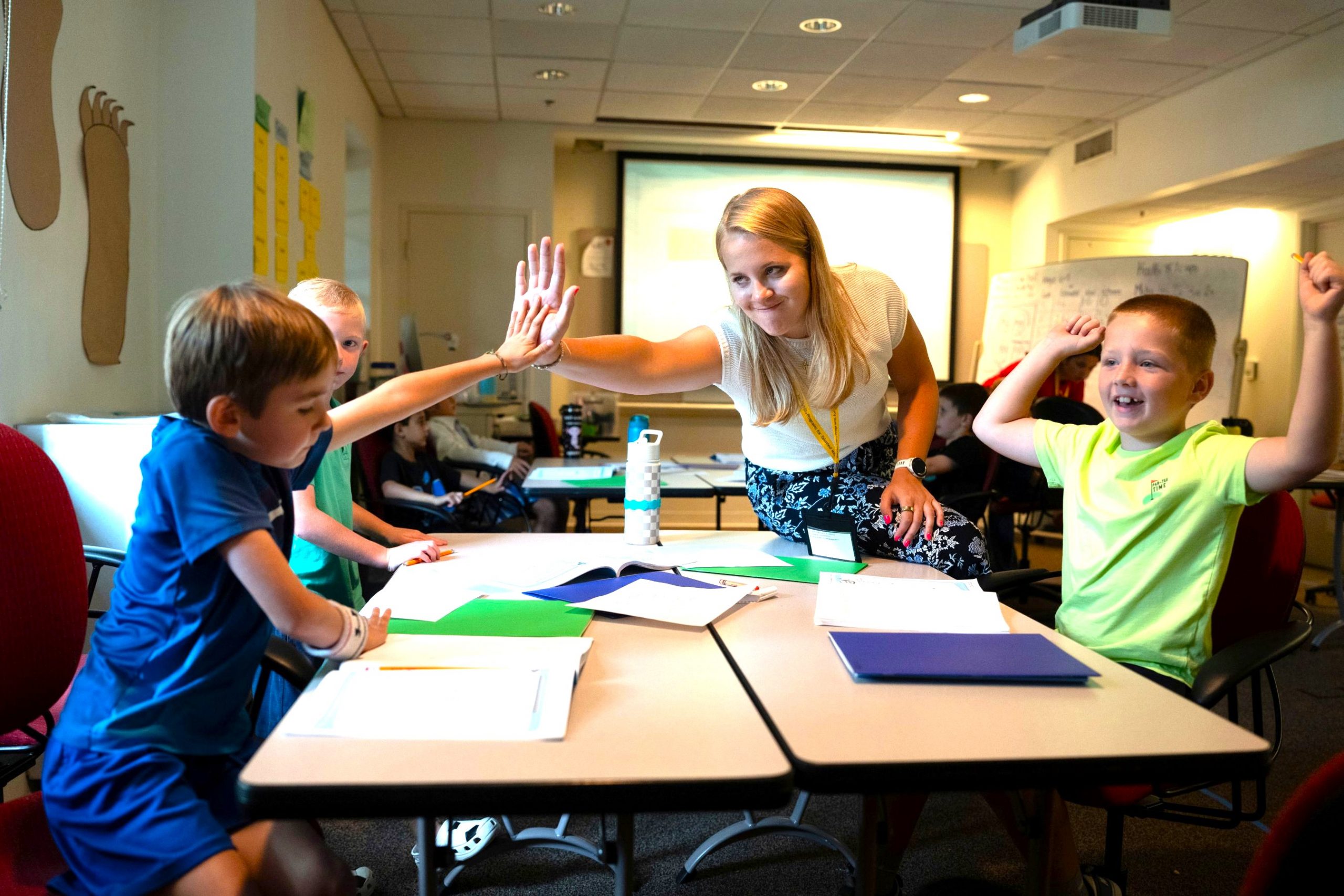 Teacher high fiving students at his desk doing group work with peers