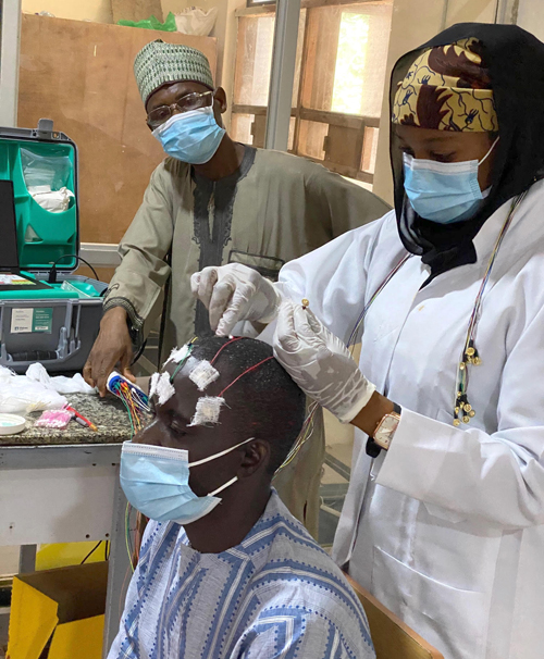 Mohammed Umar, chief EEG tech for the SEED project, supervises Community Health Workers training in EEG. Here, he looks on as Hauwa Yusuf Nuhu places EEG electrodes on Musa Sanusi Muhammad.