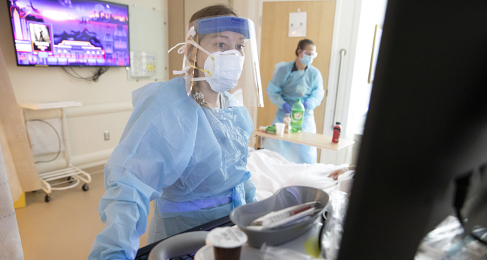 Crystal Wix, RN, foreground, and care partner Carolyn Forgac work with a patient in the COVID intensive care unit in September 2021.