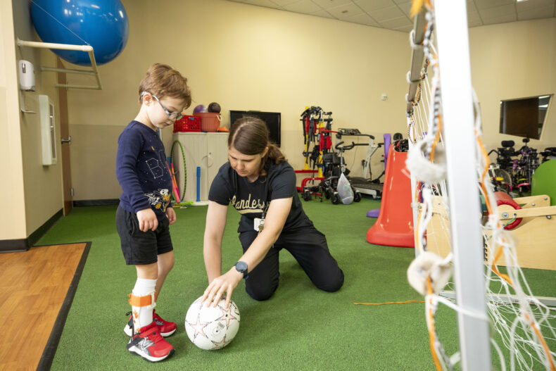 After walking on the GAITRite device, Miles Spears practices kicking a soccer ball with Beth Smith, PT, DPT. (photo by Susan Urmy)