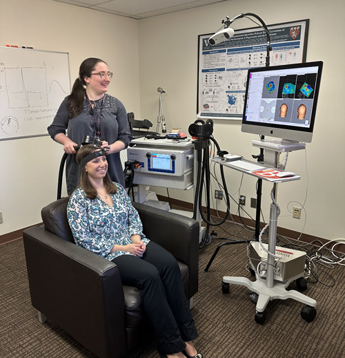 Research assistant Sophia Blyth demonstrates repetitive transcranial magnetic stimulation based on a personalized brain network map on principal investigator Heather Burrell Ward, MD.