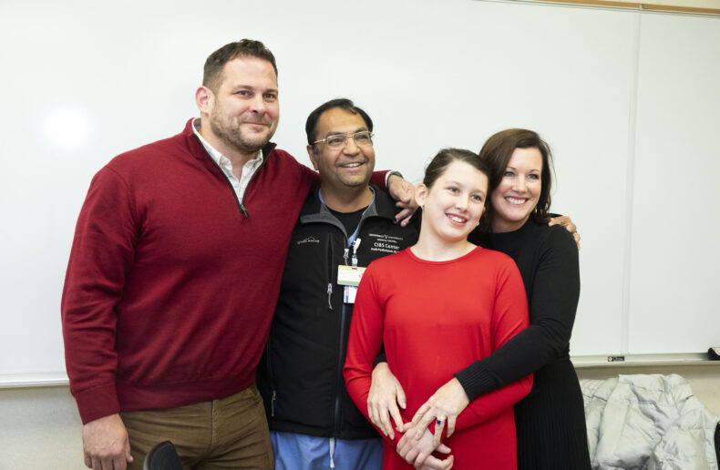 Kyle Mullicane, left, hugs his former physician, Pratik Pandharipande, MD, MSCI, along with his wife, Katie, and daughter, Harper. Pandharipande helped Mullicane understand and cope with the delirium and PTSD associated with his severe illness. (photo by Susan Urmy)