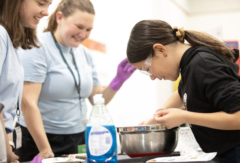 Graduate students Molly Sullivan and Brynn Roman show Violeta Morales, 10, how viruses react with soap. (photo by Erin O. Smith)