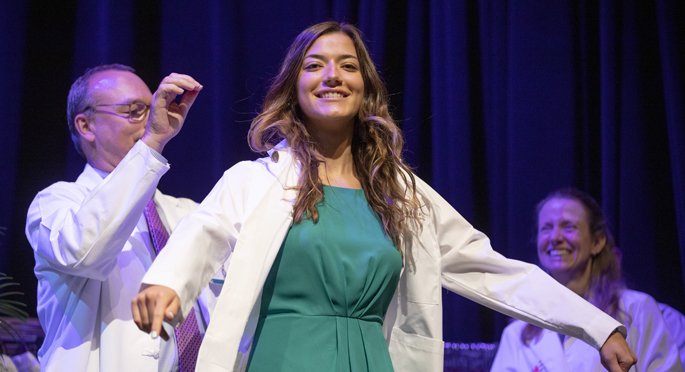 Incoming medical student Olivia Prosak receives her white coat from Jeff Balser, MD, PhD, while Amy Fleming, MD, looks on.