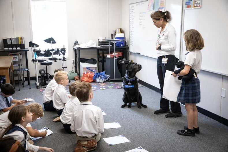 Facility dog Squid, his handler Leslie Grissim, MA, CCLS, and patient Niah Carver talk to Niah’s classmates about Squid’s role in Niah’s care. (photo by Erin O. Smith)