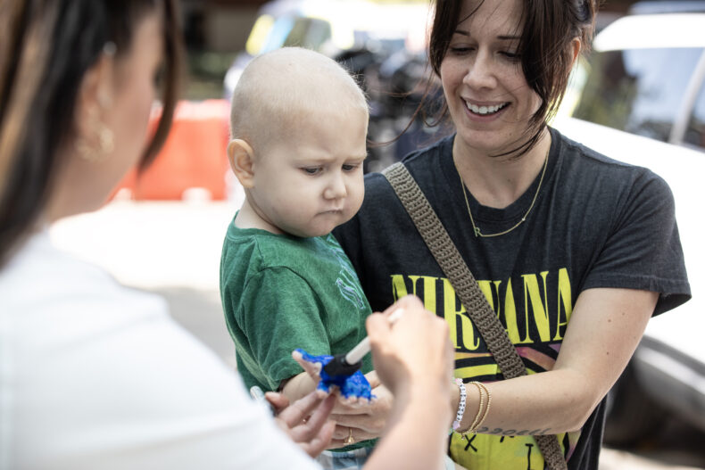 Jennifer Joyce holds her son, Roman, 3, while he gets his hand painted. (photo by Erin O. Smith)