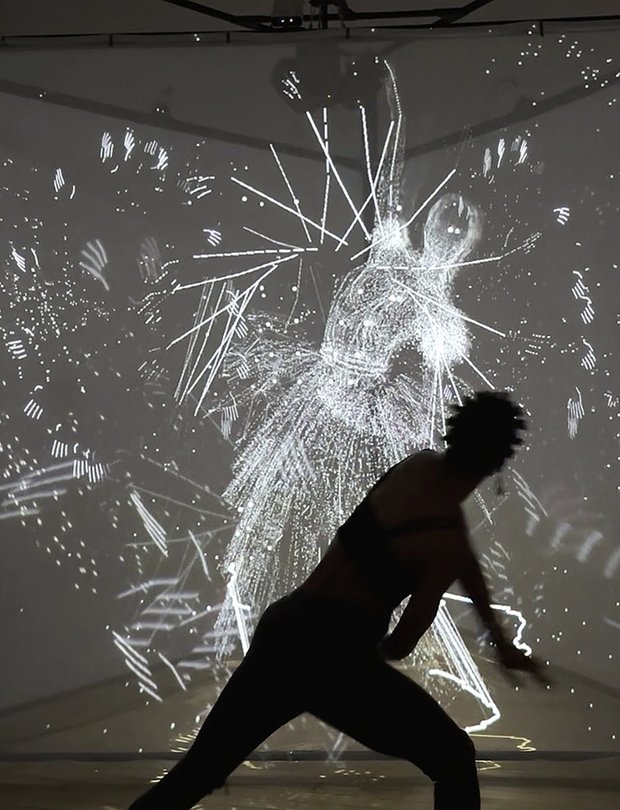 A silhouetted figure moves in front of a glowing projection of abstract, motion-reactive visuals forming a ghostly human shape.