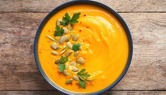 Top view of a delicious pumpkin cream soup in bowl on wooden background