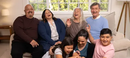 A family affected by Alzheimer's sits on the sofa together, talking and laughing.