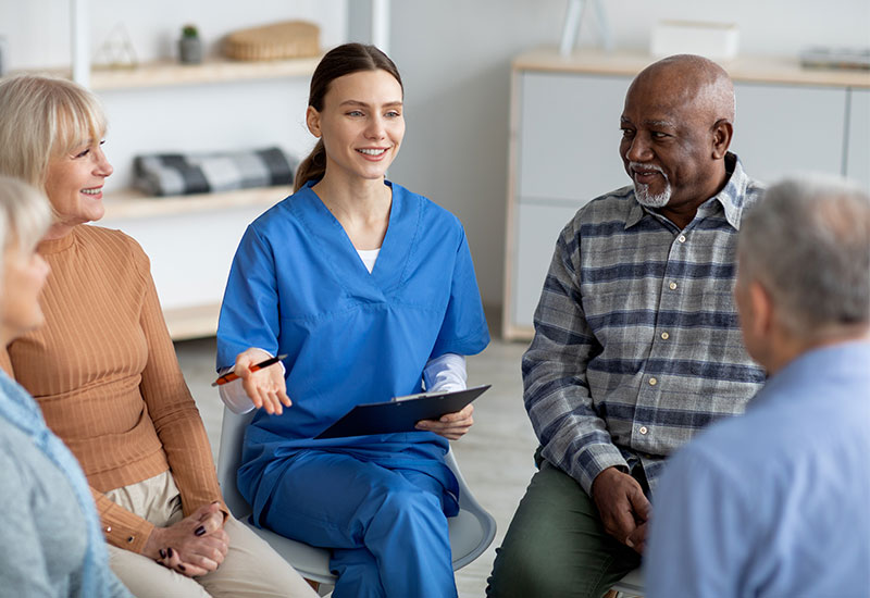 A female medical professional sits in a group of male and female individuals to have a discussion