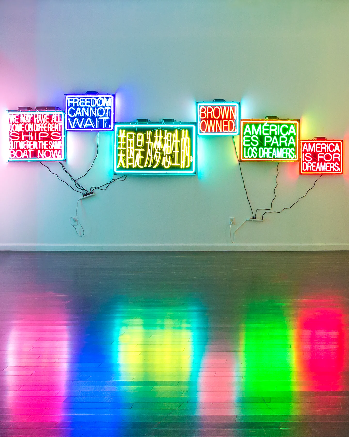 Five colorful neon signs hang on the wall with messages that include, "Freedom cannot wait," "Brown owned," and "America is for Dreamers."