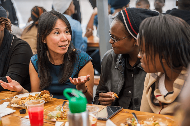 Three people talking and sharing a meal at a large table during a Ventures event.