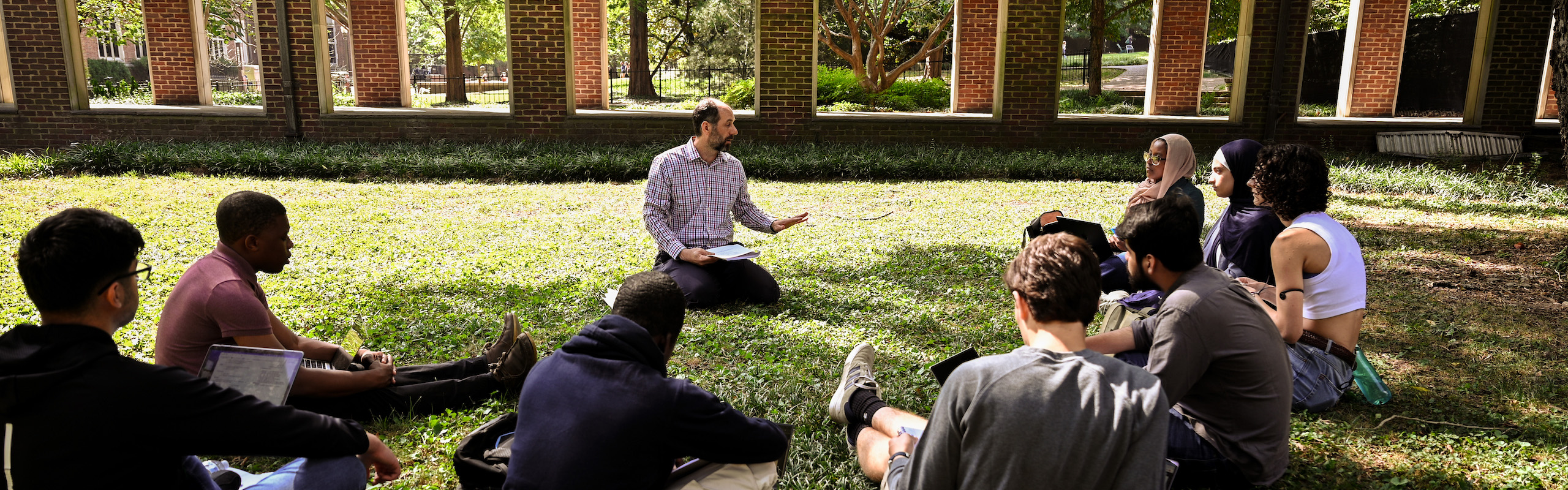 Religious studies class sitting on the ground outside listening to professor