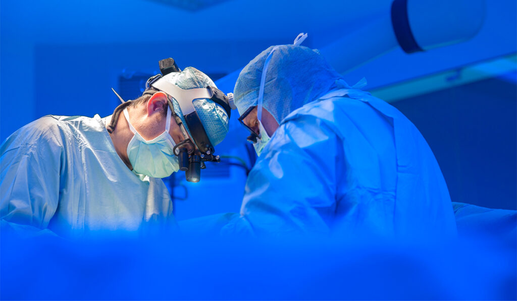 Surgeons in surgical suite with patient obscured. Blue overtones