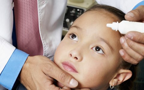 A doctor putting eye drops in a girl's eye