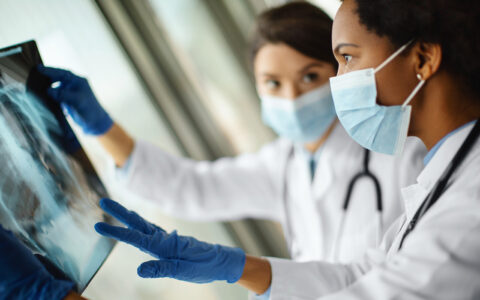 Two healthcare workers wearing masks and gloves examine chest X-ray