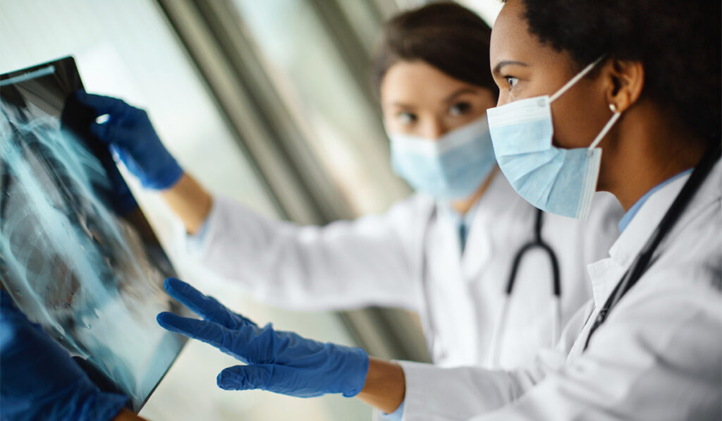 Two healthcare workers wearing masks and gloves examine chest X-ray