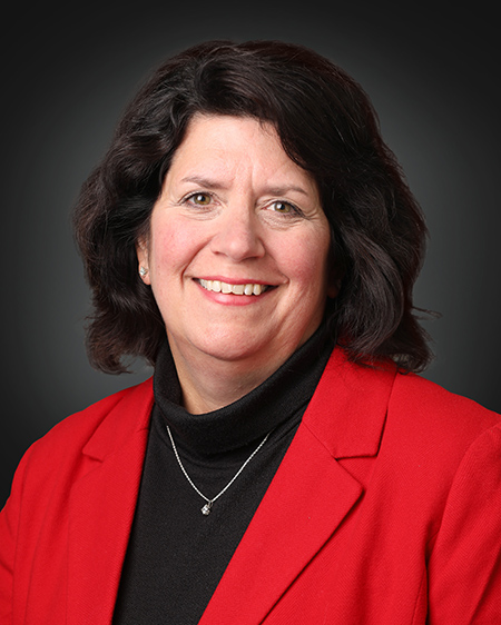 Portrait of Cynthia Baldwin, M.S., R.N., dark hair, red coat, over black shirt