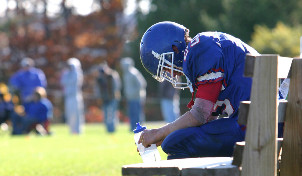Football player on the bench with head down