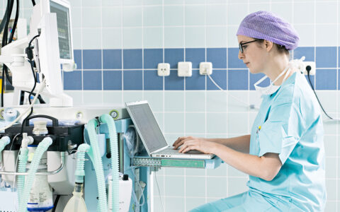 Healthcare worker wearing protective gear sits down to record notes on a laptop computer