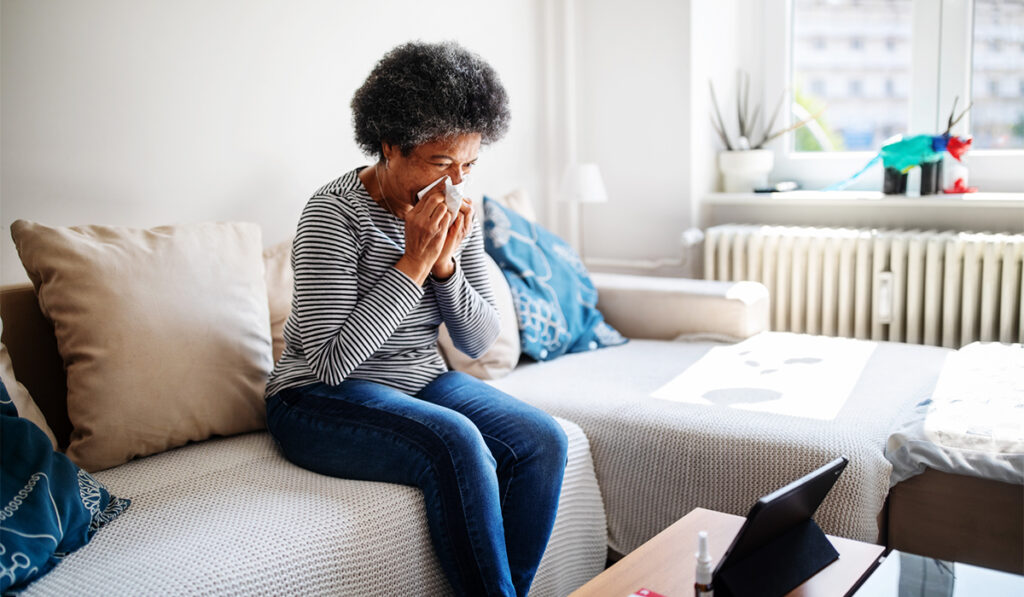 Woman sitting on a coach and blowing her nose