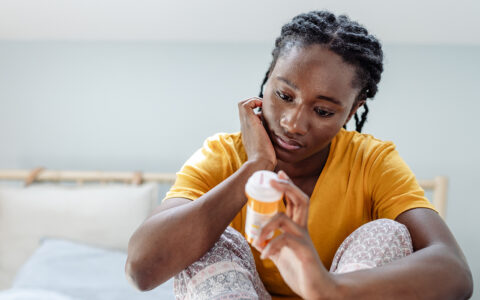 Young African American woman in bedroom looking somberly at prescription pill container
