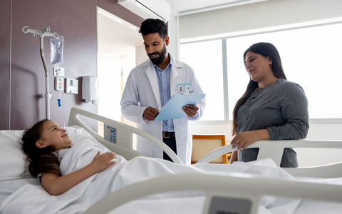Mother and doctor smiling at a happy young girl lying down in a hospital bed