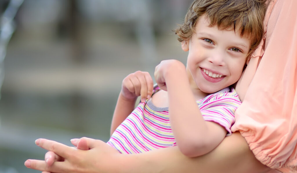 Close-up portrait of beautiful smiling disabled child in the arms of mother.