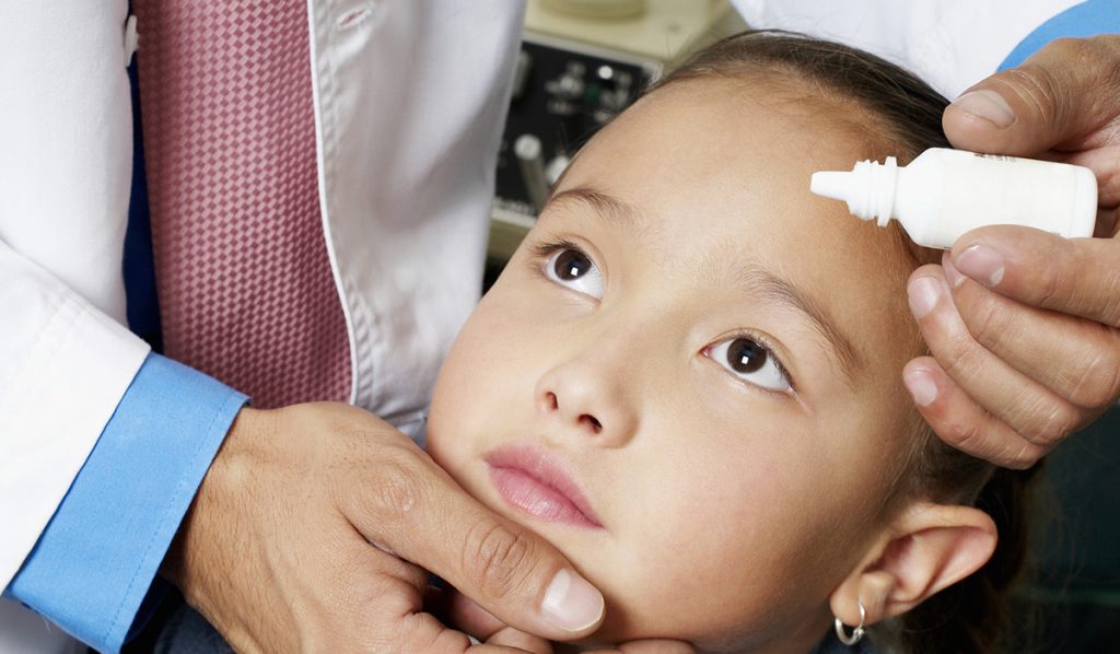 A doctor putting eye drops in a girl's eye