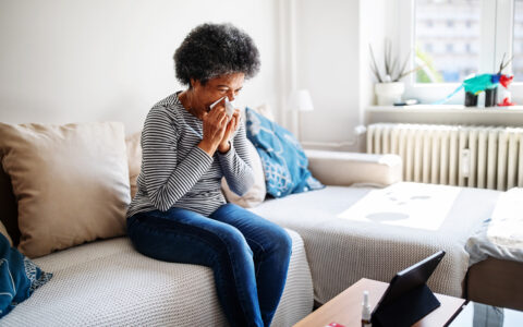 Woman sitting on a coach and blowing her nose