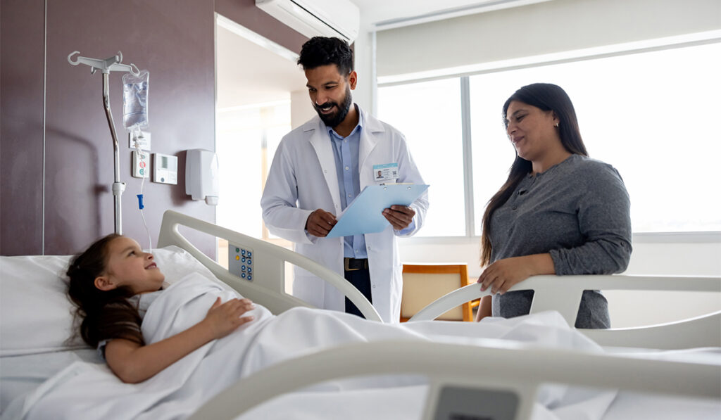 Mother and doctor smiling at a happy young girl lying down in a hospital bed