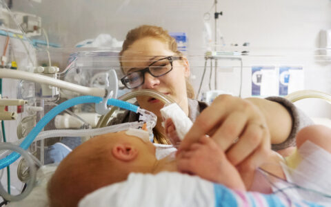 Woman holding finger of a baby in the NICU